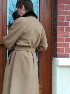 femme ouvrant la porte en manteau beige
