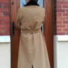 femme de dos en manteau beige devant porte d'entrée