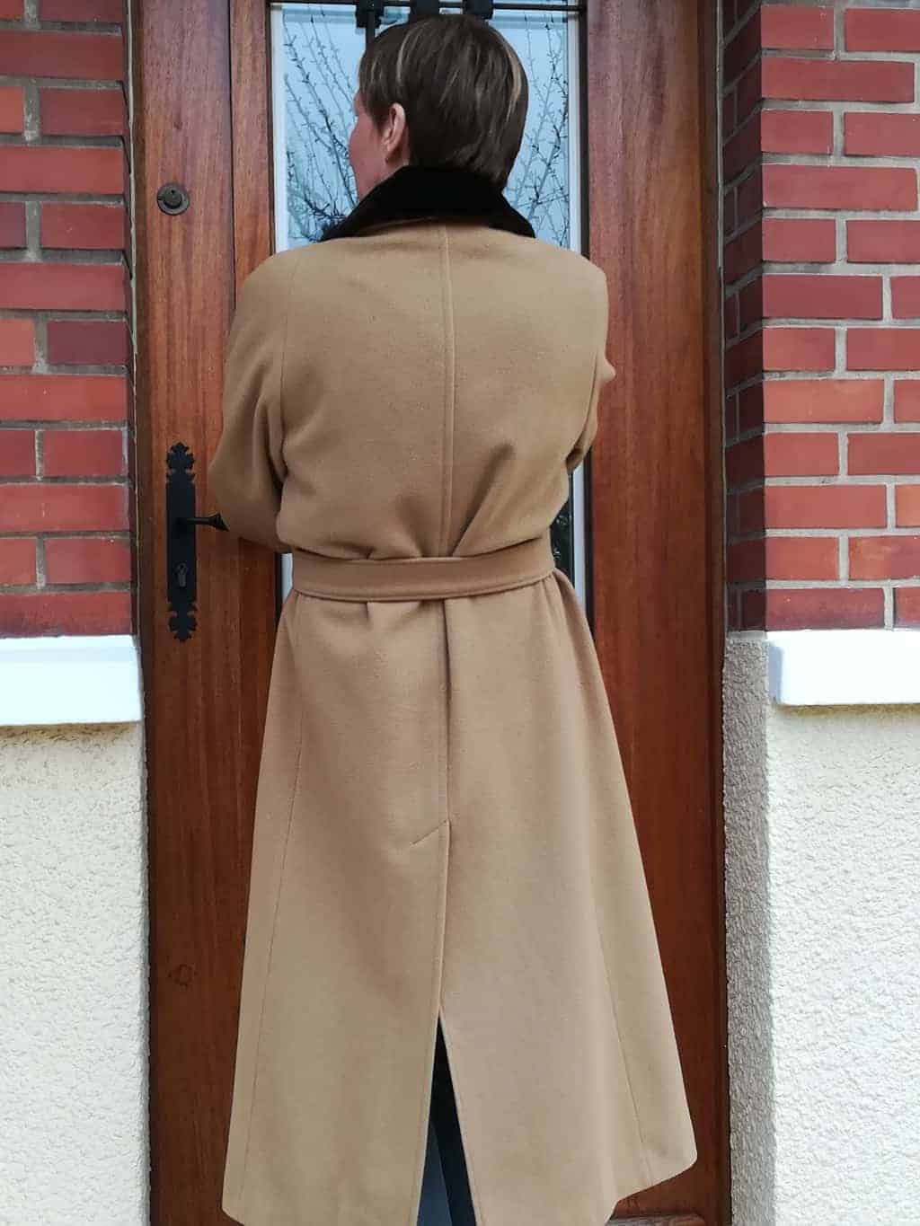 femme de dos en manteau beige devant porte d'entrée